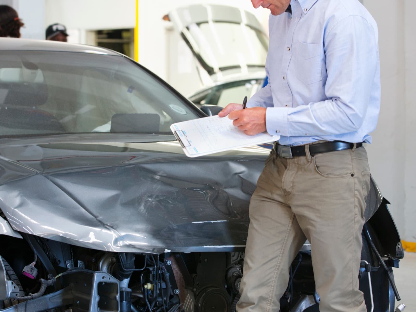 Man inspects damaged car and writes notes.