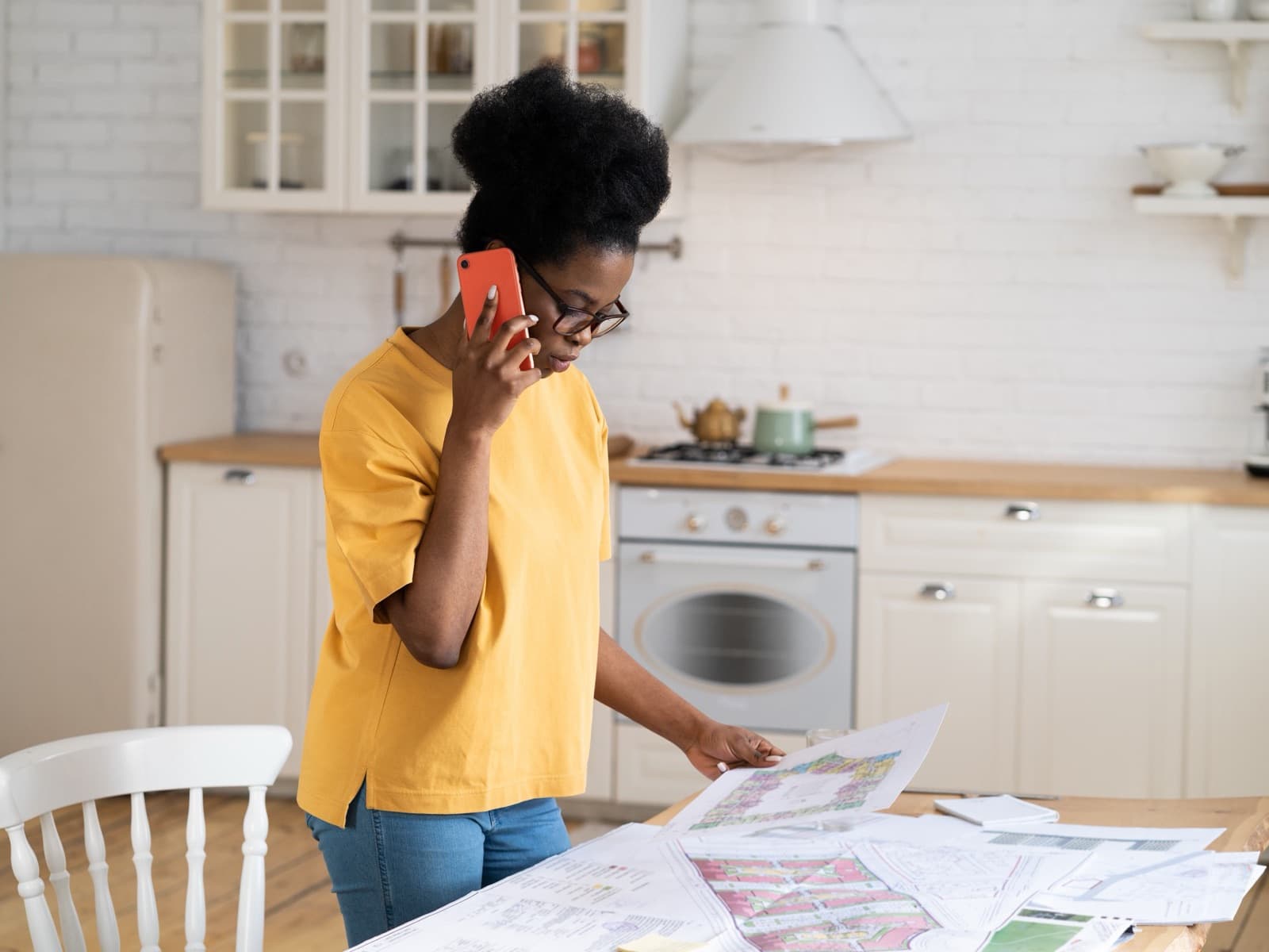 Woman on phone over plans in kitchen.