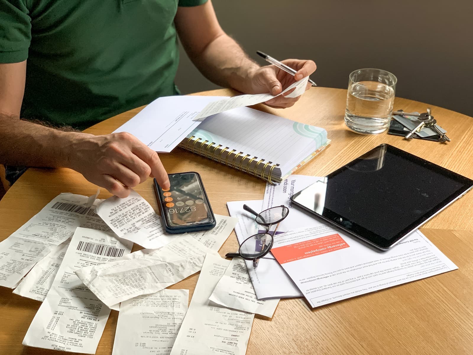 Hands working out bills on a phone calculator beside receipts.